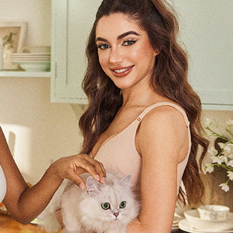 Woman wearing beige camisole holding a fluffy white cat in a kitchen setting.