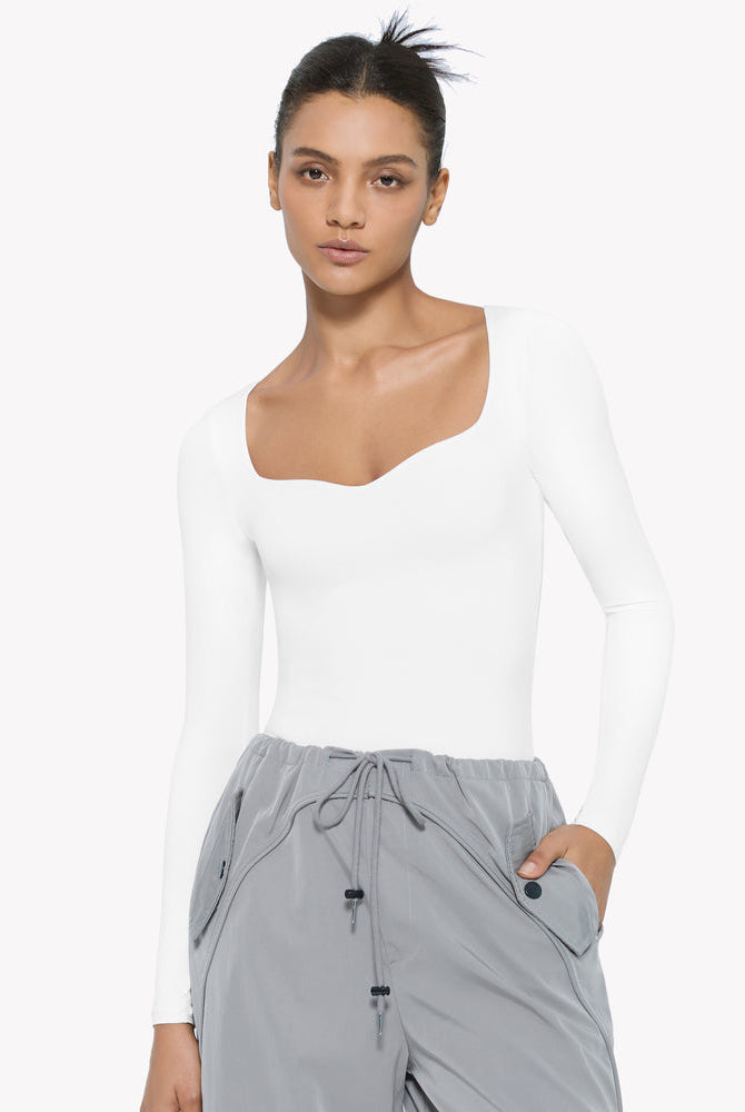 White sweetheart neckline long sleeve bodysuit shapewear, model wearing gray pants, premium comfort