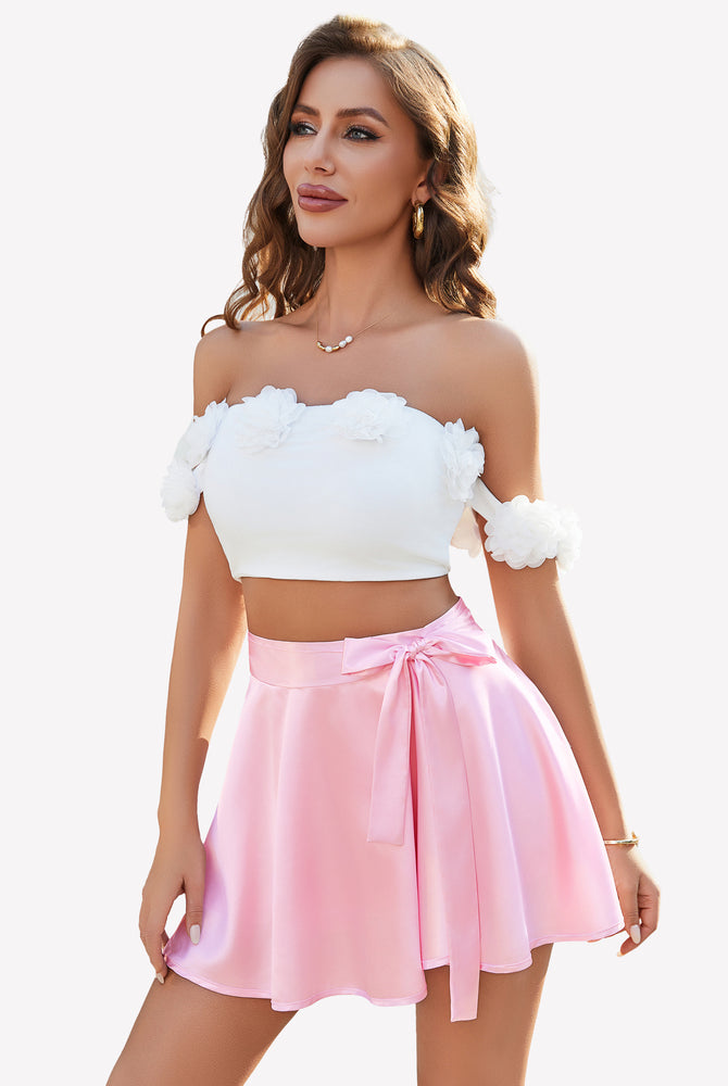 Pink satin mini skirt with bow and white floral crop top, ideal for casual wear