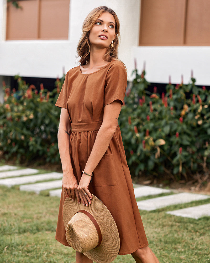 Brown midi dress with short sleeves and pockets. Woman holding a straw hat.