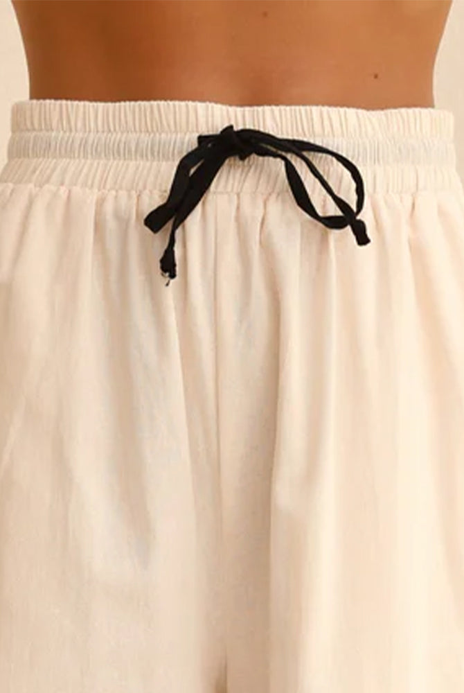 Beige linen pajama shorts with elastic waist and black drawstring bow.