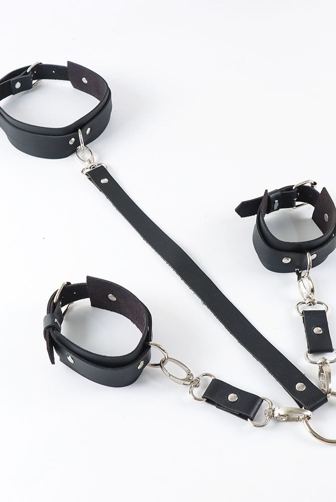 Black leather wrist cuffs, neck collar, and connecting strap with silver metal rings.