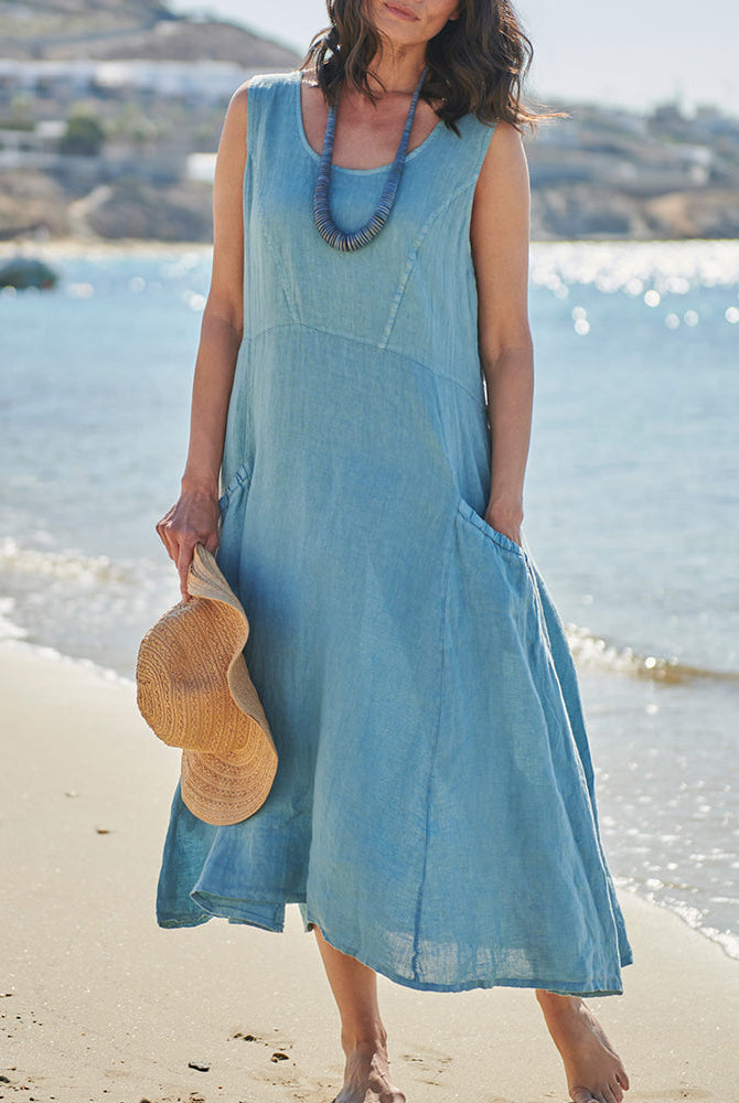 Light blue sleeveless linen vacation dress with pockets on a woman at the beach, perfect for summer.