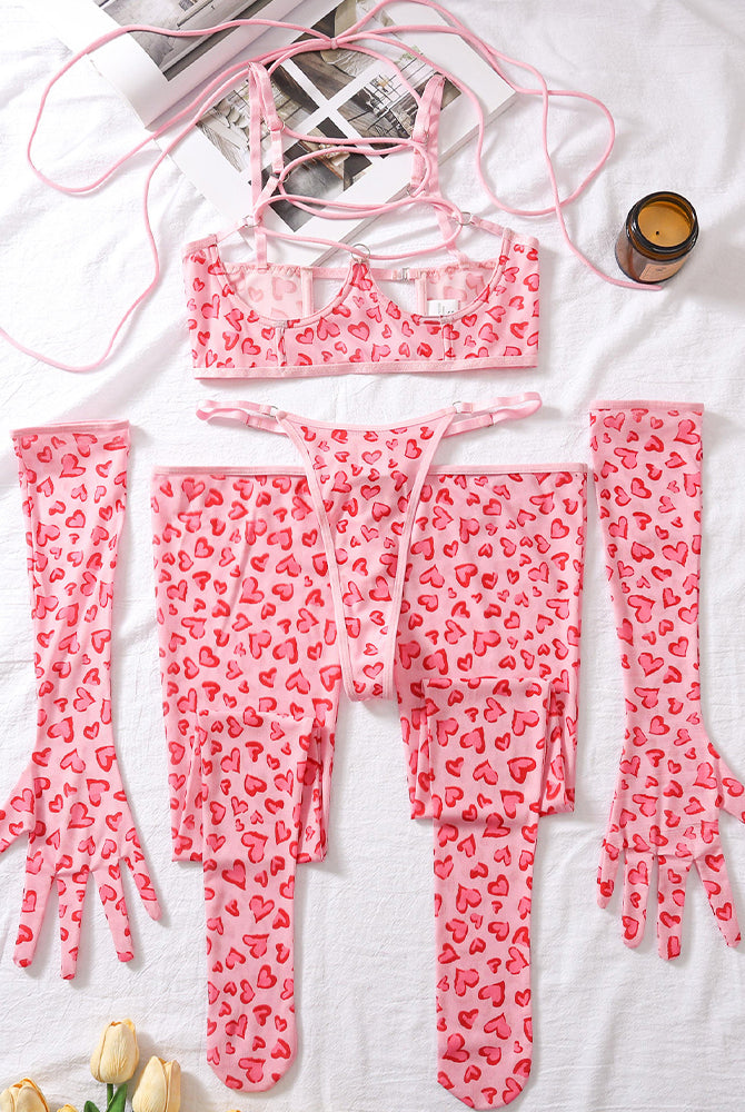 Pink heart-pattern lingerie set laid flat: lace-up mesh bra, thong, and long leg socks