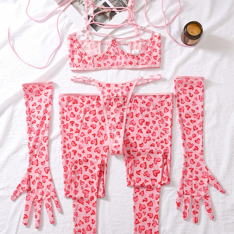 Pink heart-pattern lingerie set laid flat: lace-up mesh bra, thong, and long leg socks