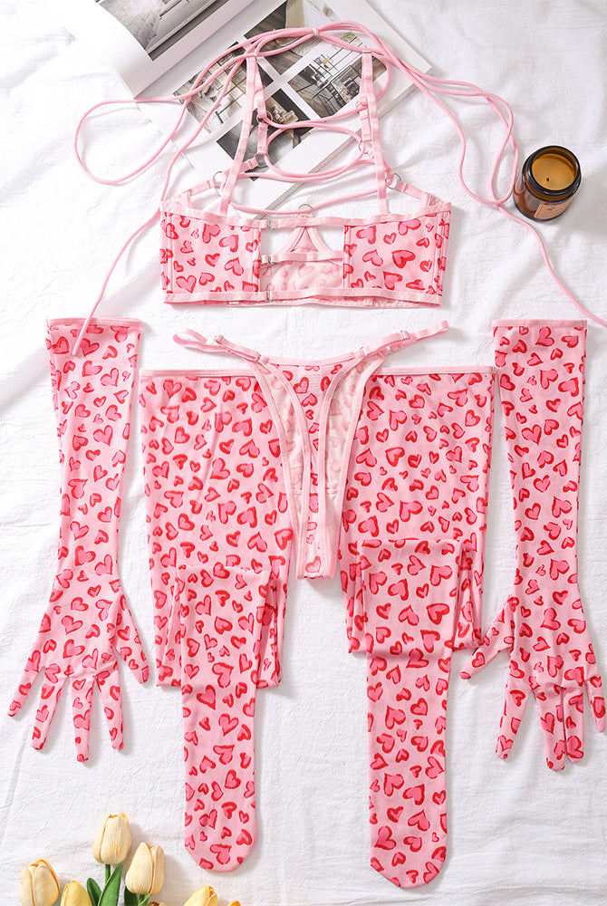 Pink heart-pattern lingerie set laid flat: mesh bra, tie-front thong, arm warmers, leg socks