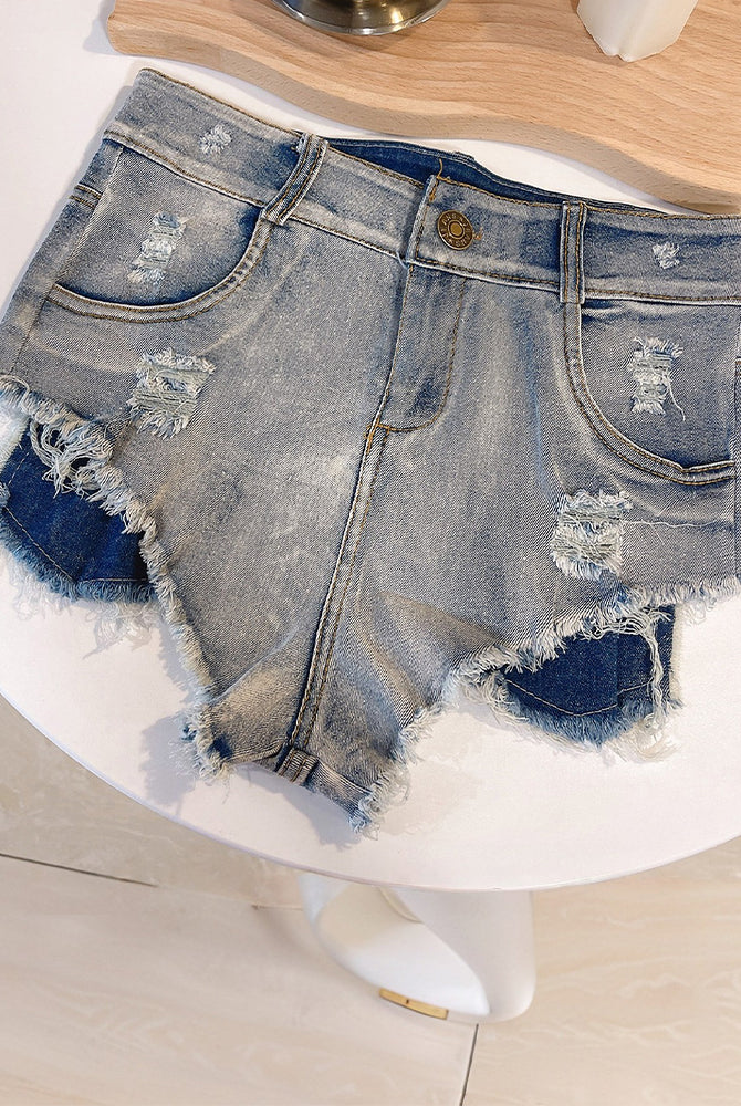 Light blue high-waisted distressed denim shorts laid flat, frayed hem and patch rips