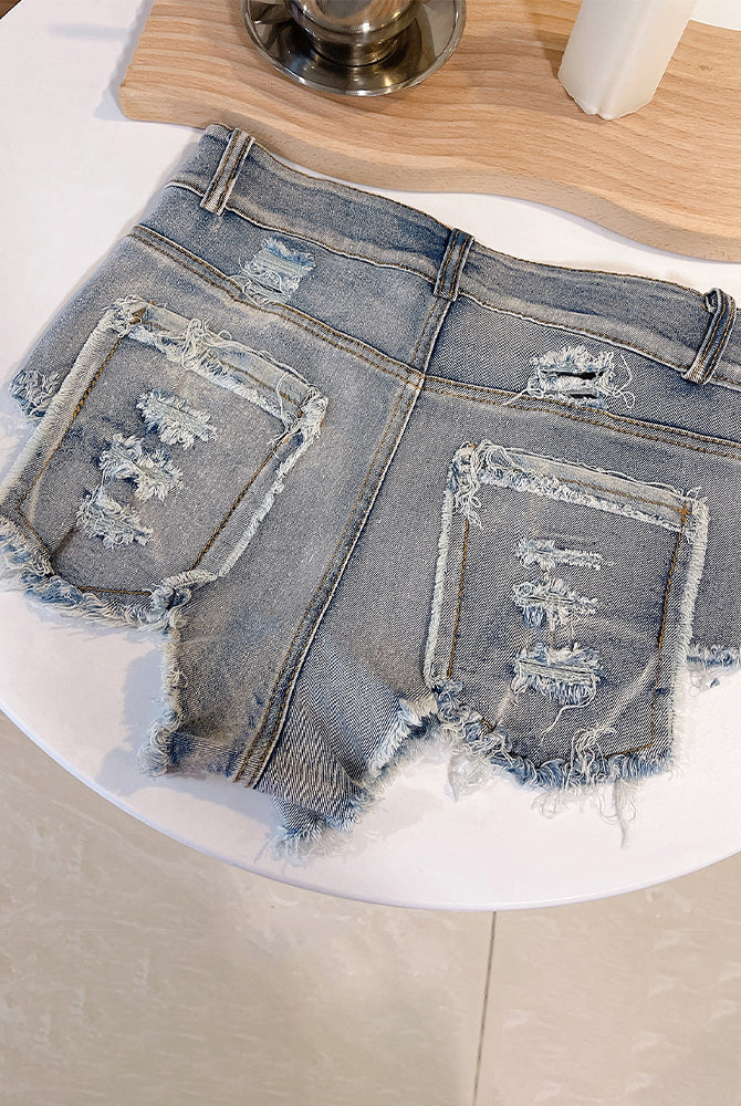 Light blue high-waisted distressed denim shorts flat on table, back rips and frayed trim
