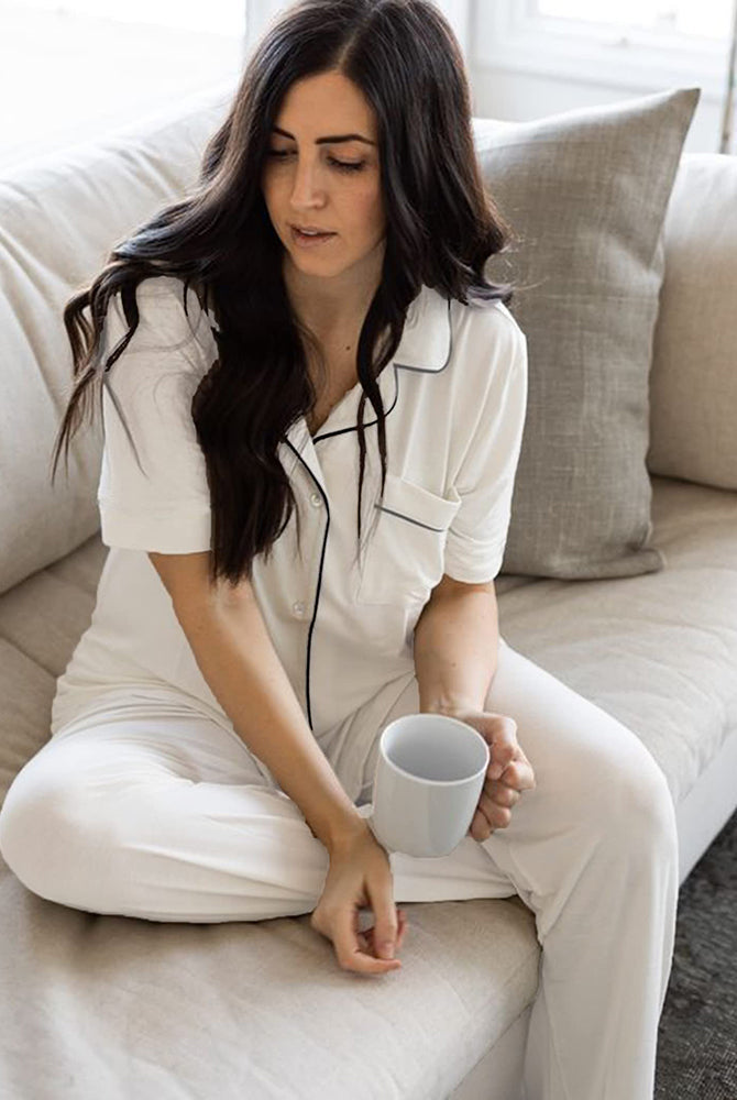 White button-down pajama set with black trim. Comfortable sleepwear for women, holding a mug.