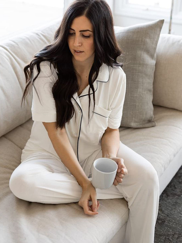 White button-down pajama set with black trim. Comfortable sleepwear for women, holding a mug.