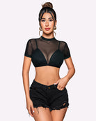 Pink see-through crop top with integrated bra and open back styled with black denim shorts.