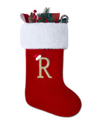 Red velvet Christmas stocking with white plush cuff, gold R monogram, and greenery tucked inside.