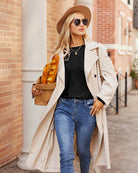 Woman in black top, blue jeans, and beige trench coat, holding bread, casual wear