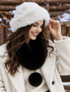 Black faux fur collar scarf with a matching pom-pom, worn beneath a white fur hat.