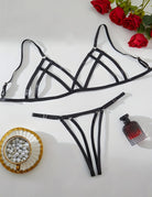 Black strappy bra and thong set laid flat, showing the open cup design