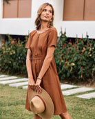 Brown midi dress with short sleeves and pockets. Woman holding a straw hat.
